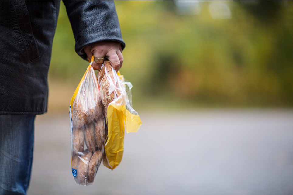 Käsivarsi ja käsi, joka pitelee kahta leipäpussia. Taustalla tie ja puita.