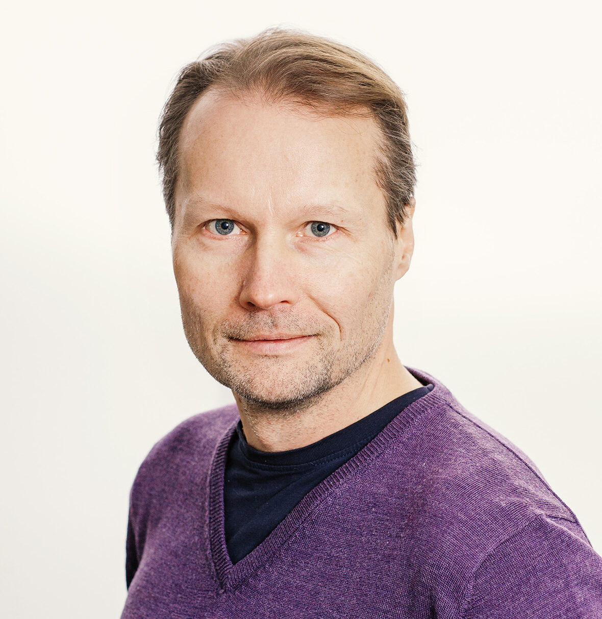 Lyhyttukkaisella miehellä on ohuenohut parta ja vee-aukkoinen pusero.