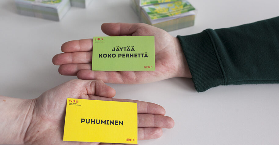Kaksi kättä pitelee kortteja "jäytää koko perhettä" ja "puhuminen".