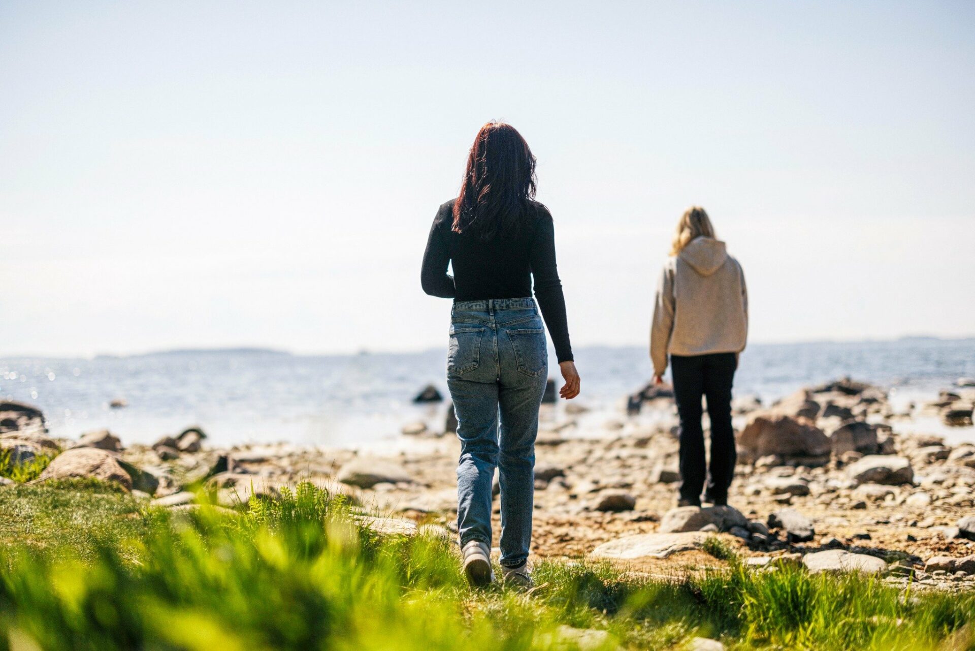 Rannalla kaksi nuorta selin. Tummahiuksinen kulkee kohti etäällä olevaa vaaleatukkaista tyttöä.
