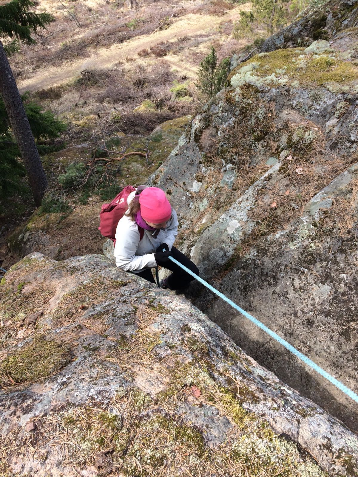 Ihminen kiipeää kapeassa kalliorailossa köydestä kiinni pitäen.