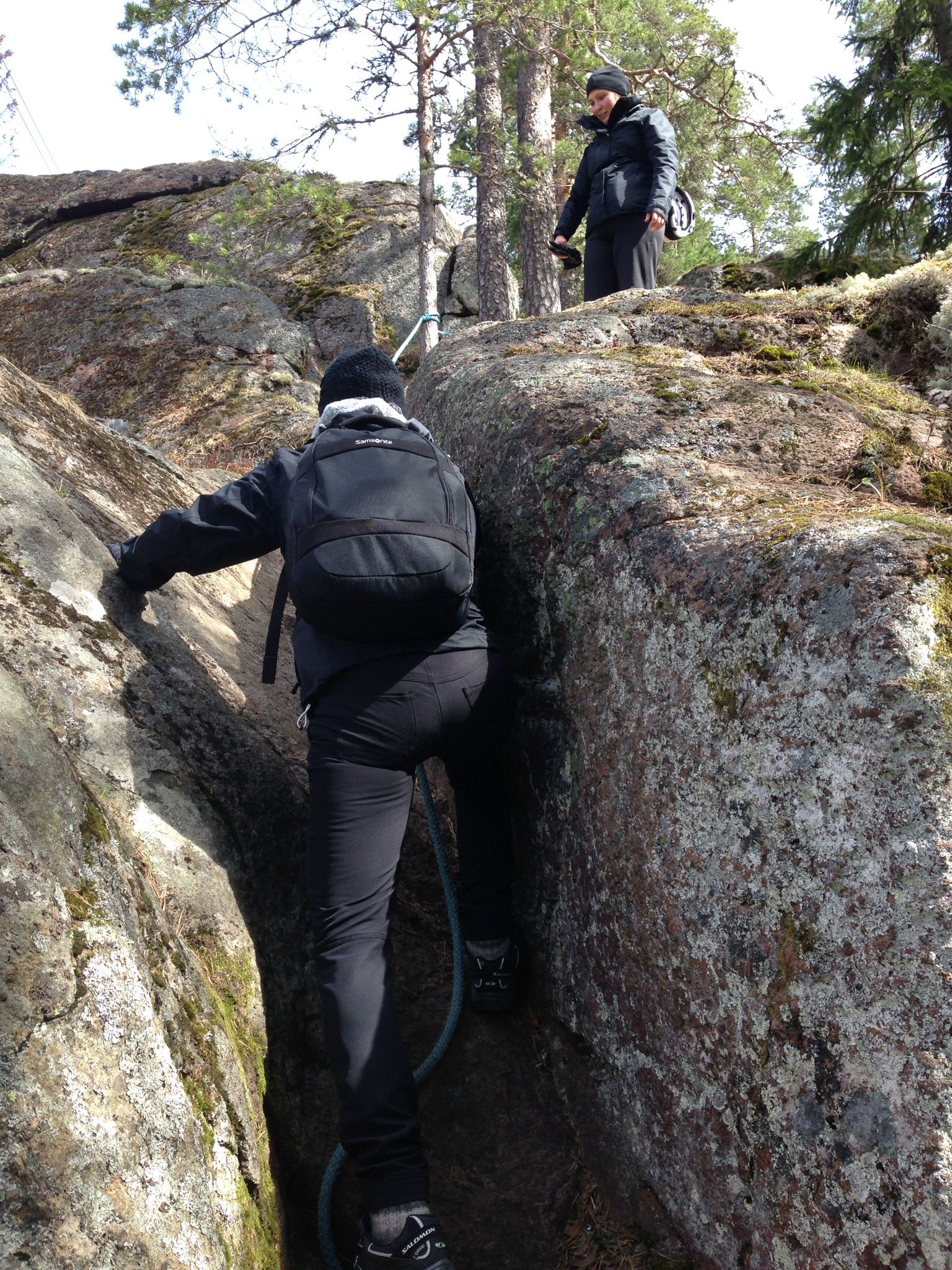 Ihminen kiipeää kapeassa kalliorailossa. Toinen ihminen odottaa ylempänä.