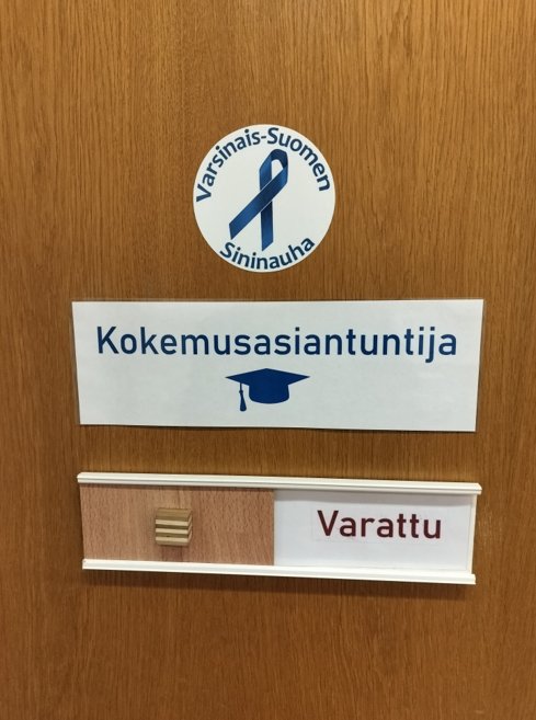 Varsinais-Suomen Sininauhan logo, jossa on teksti ympyrämuodossa Varsinais-Suomen Sininauha. Ympyrän sisällä on sininen nauha lenkillä. Logon alla on teksti kokemusasiantuntija ja sana varattu.