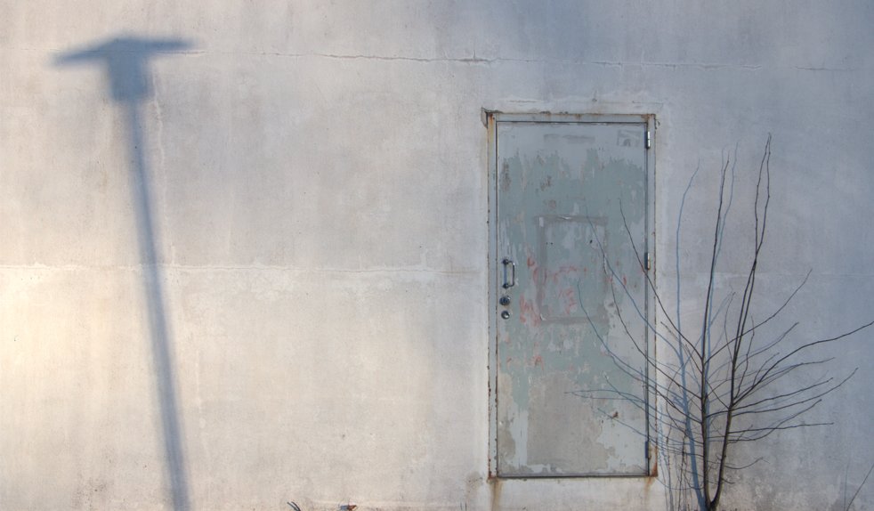 Oikealla seinässä on ovi ja vasemmalla on lyhtypylvään varjo.