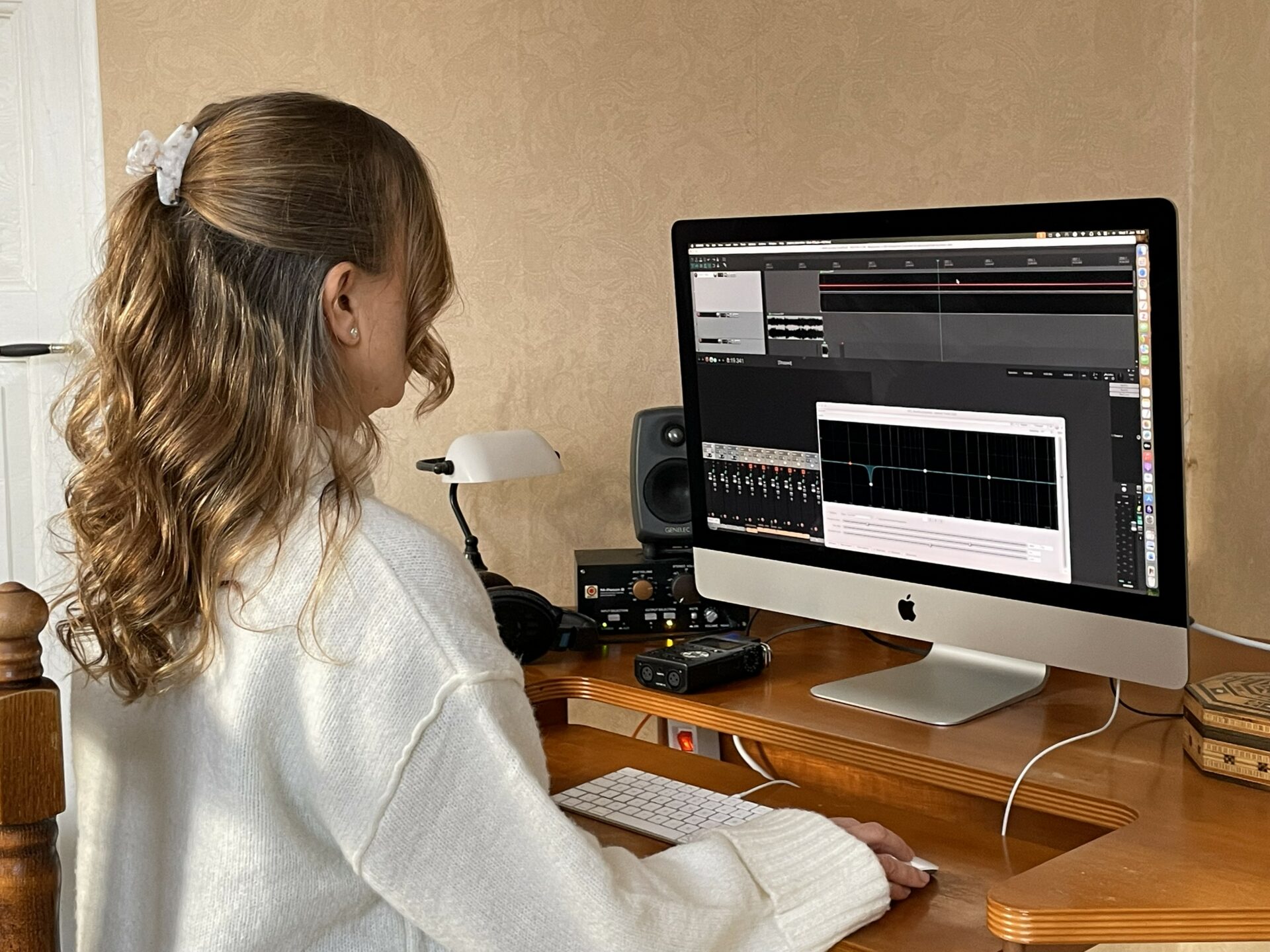 Pitkähiuksinen nainen istuu ison tietokoneruudun edessä. Ruudussa näkyy ääniaaltoja.