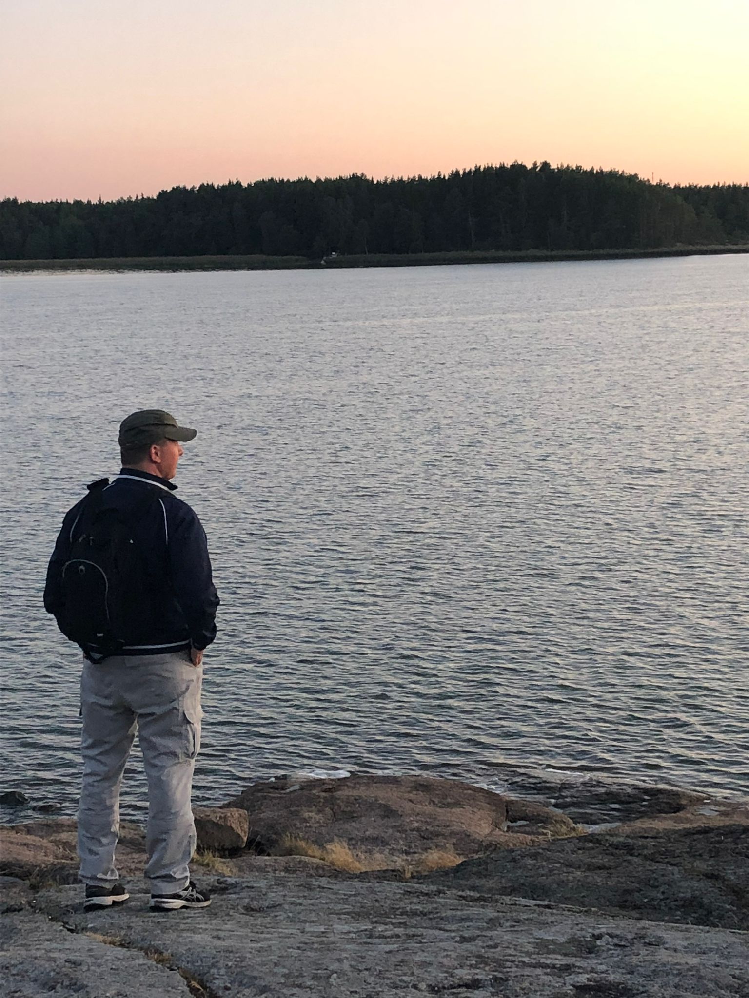 Mies seisoo yksin meren rannalla. Taustalla on saari.