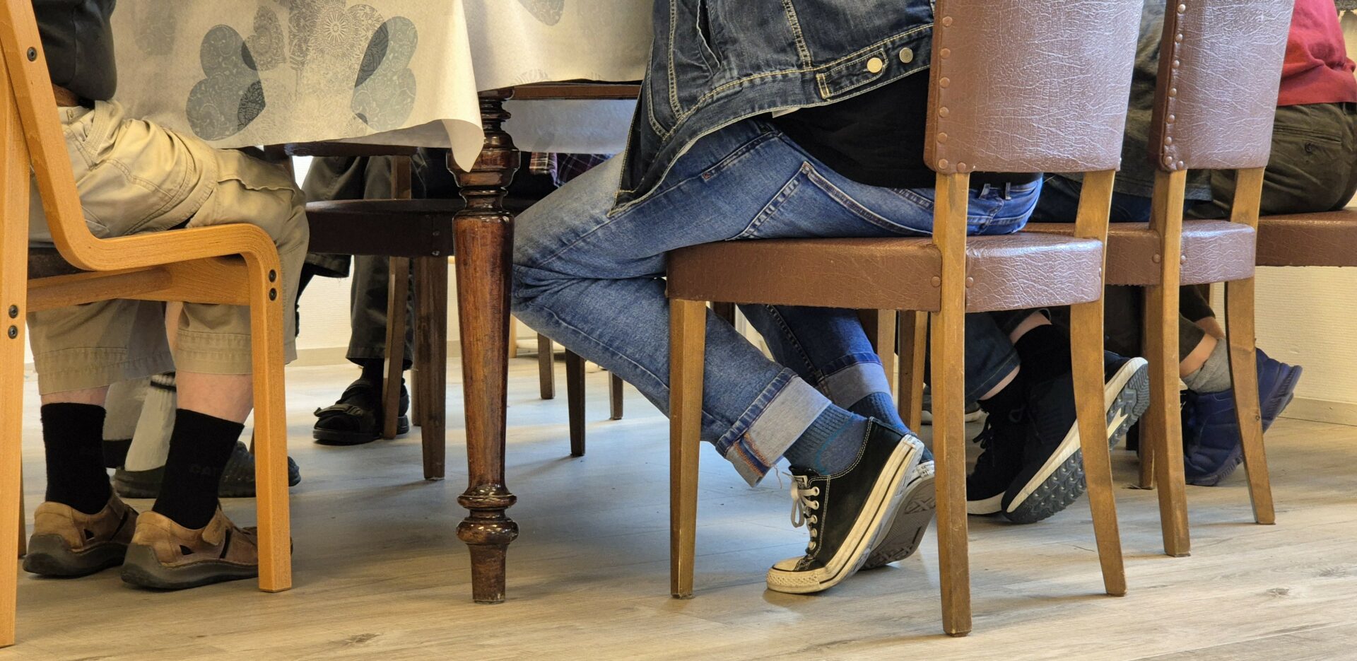 Ihmisiä istuu tuoleilla pöydän ääressä, heistä näkyy vain jalat.