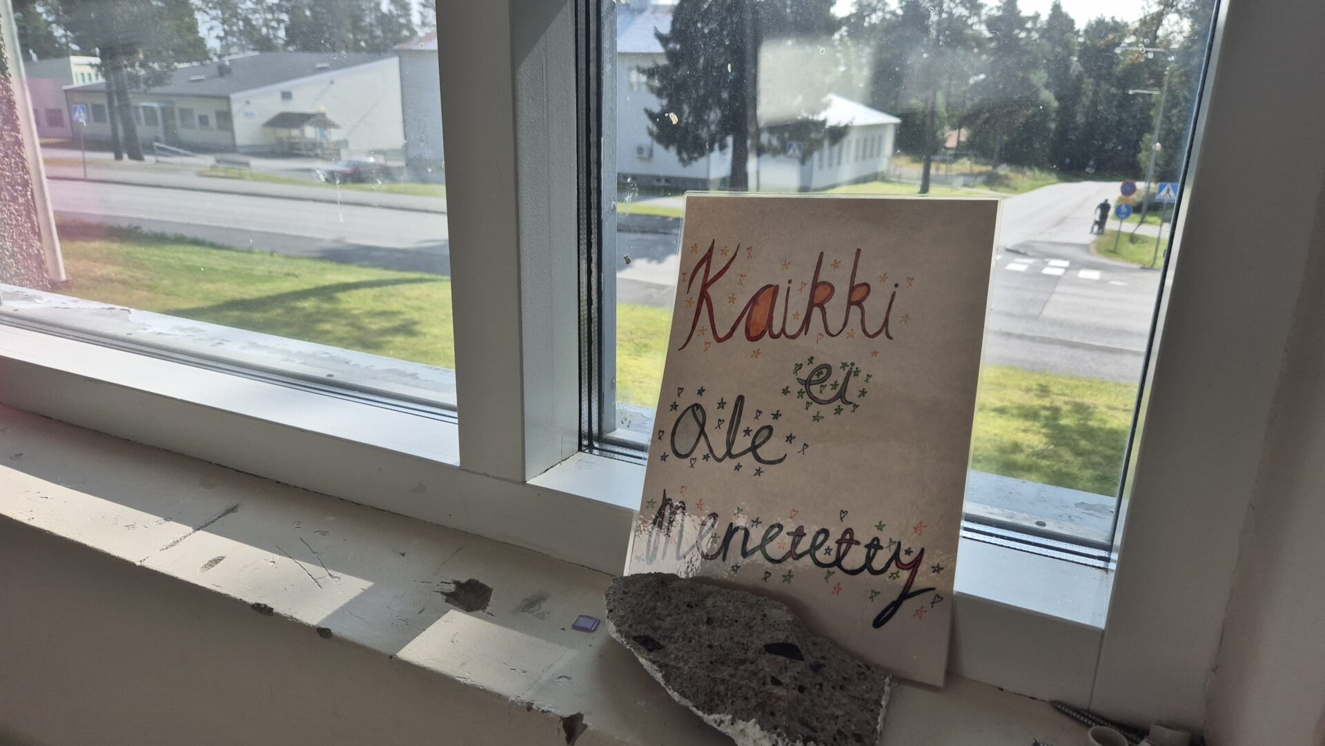 Ikkunalaudalla on paperi, jossa on värikynillä kirjoitettu teksti: Kaikki ei ole menetetty.