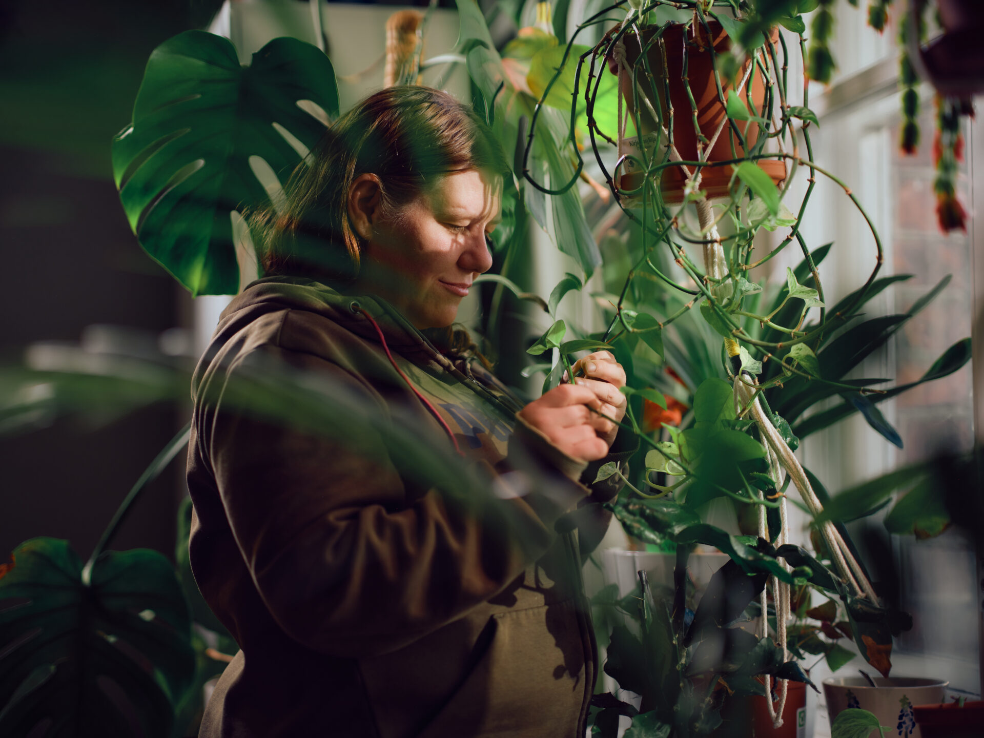 Pitkätukkainen nainen on sivuttain riippuvien kasvien keskellä.