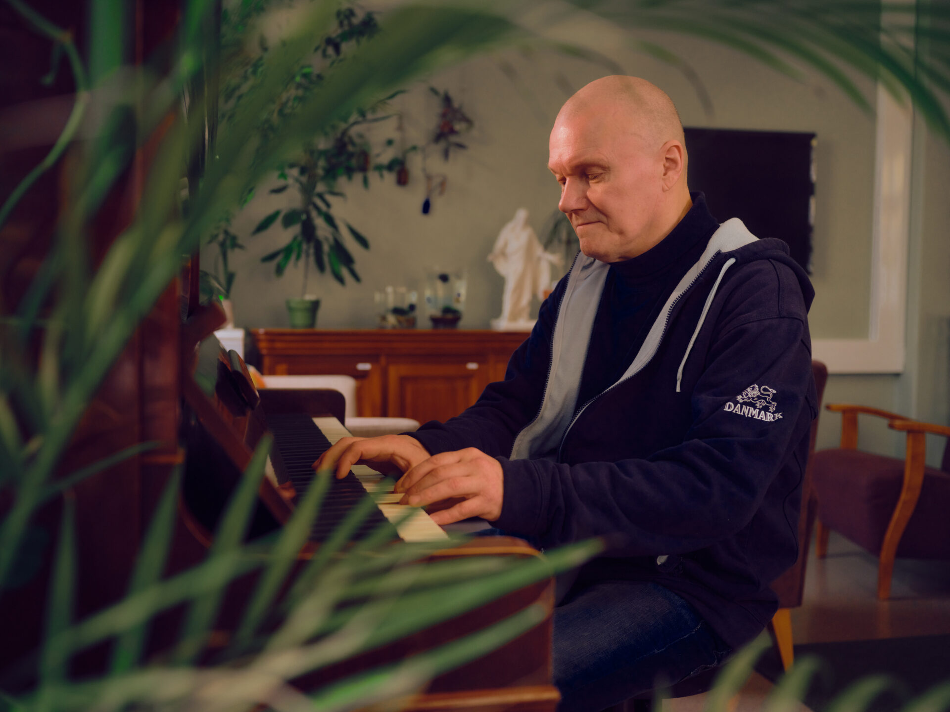 Vakava, kalju mies soittaa pianoa. Etualalla on vihreitä kasvin lehtiä