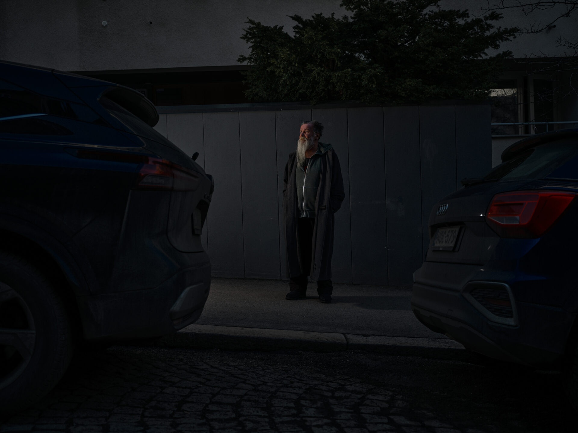 Pimeällä kadulla kahden auton välissä on iäkkään miehen hahmo.