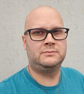 Silmälasipäinen, kalju, vakava mies, jolla on tee-paita.